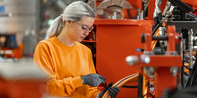 A woman in work clothes putting together machine cables in an industrial environment