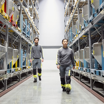 A man and a woman in work clothes walking between two warehouse shelves