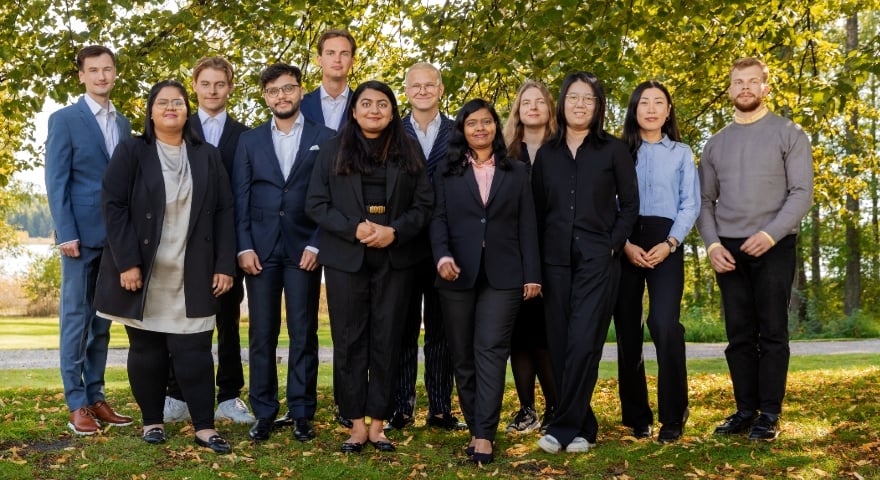 Twelwe persons standing in a group looking in to the camera in an outside autumn environment