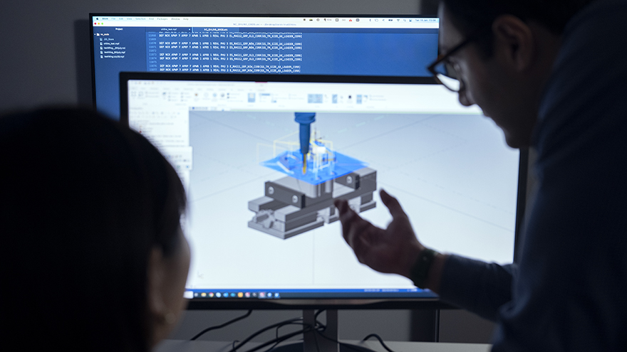 The heads of a woman and a man next to a computer screen displaying software simulating machining operation