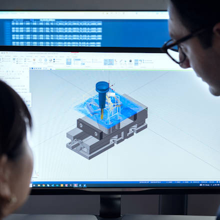 A woman and a man looking at a computer screen with an image of a toolpath for a milling operation which is generated using CAM software
